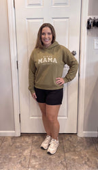 Woman wearing a Kiksy Mama Est 2026 hoodie with distressed white varsity lettering.