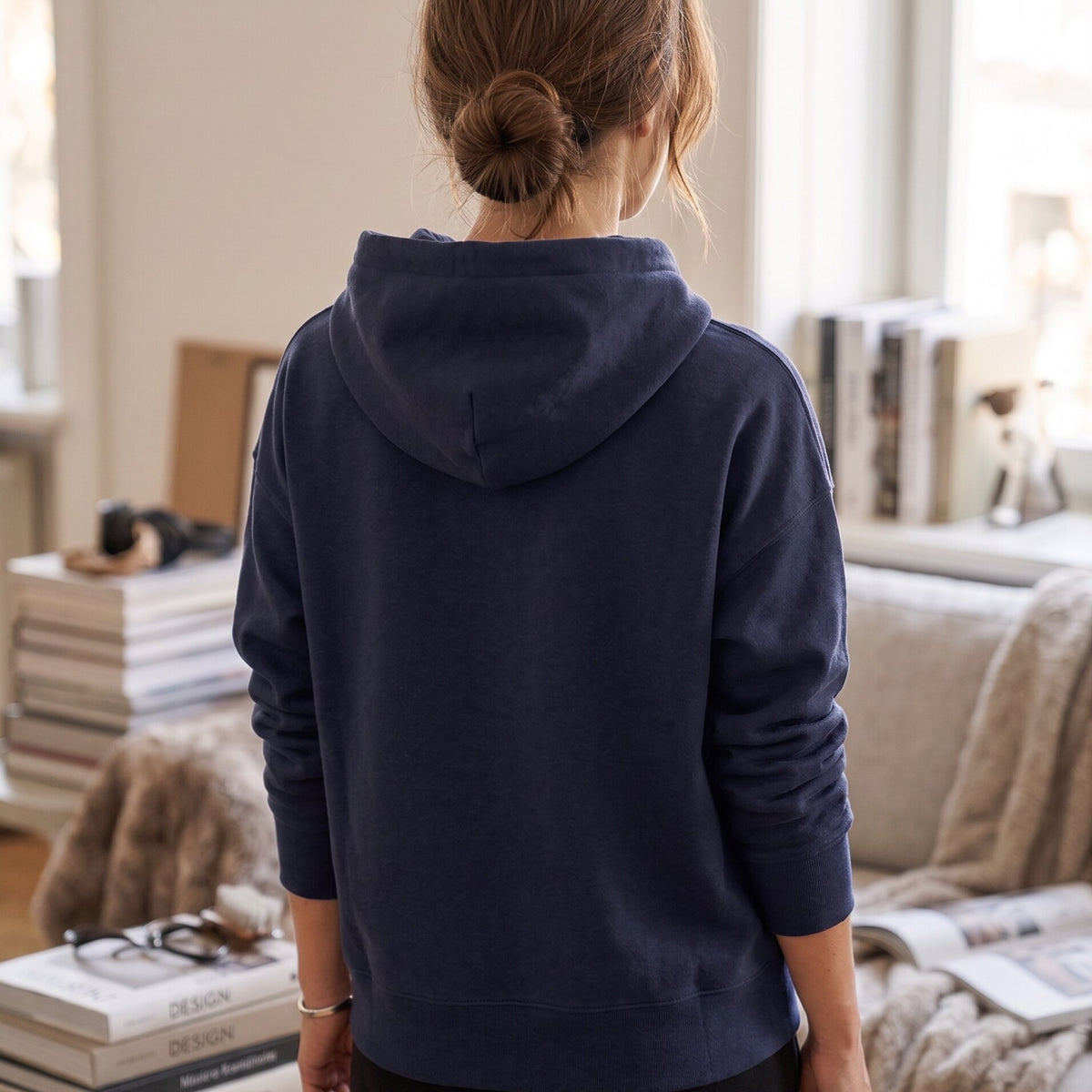 Woman wearing Kiksy dark blue hoodie featuring the text Proud Sponsor of a very messy LIVING ROOM